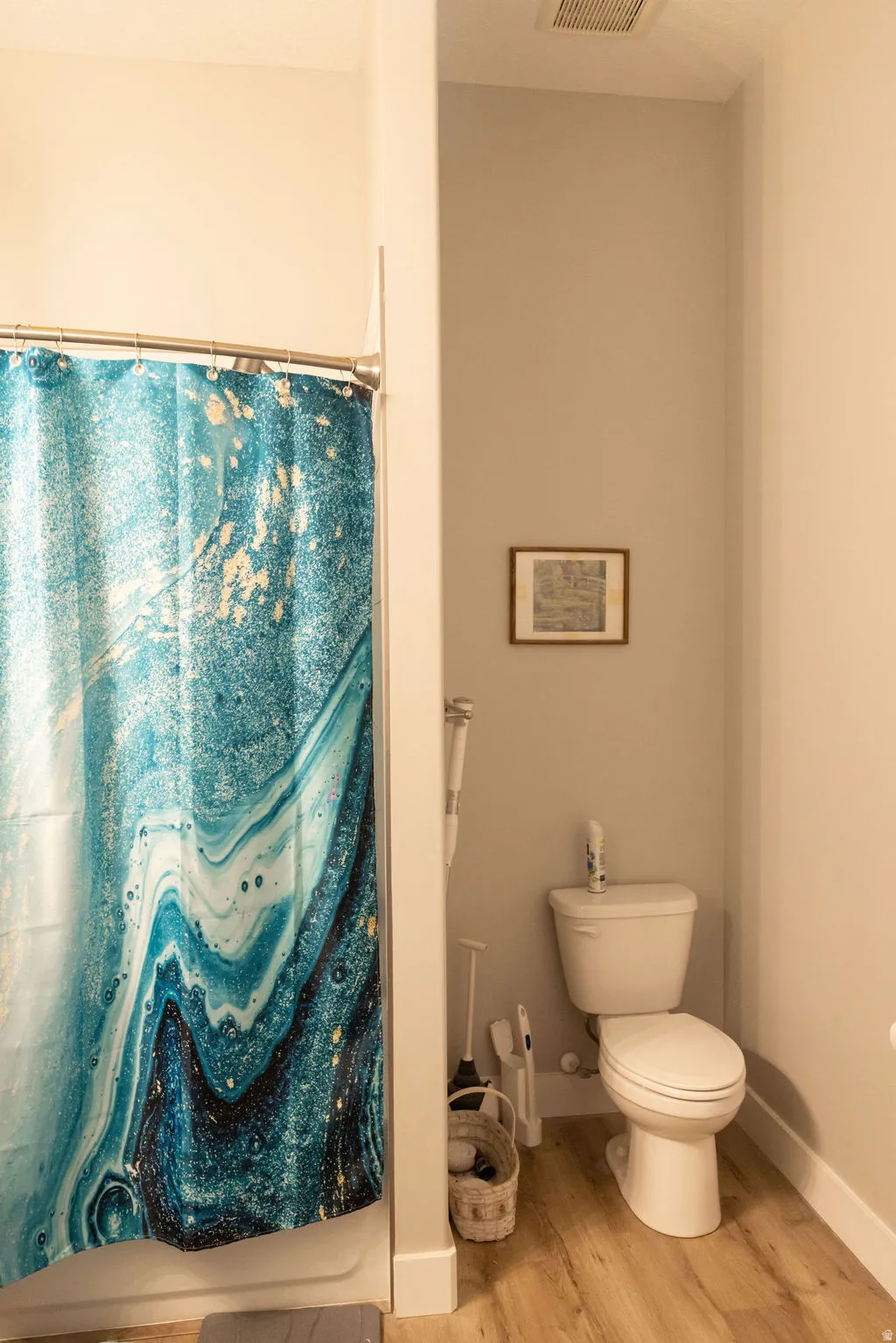White toilet, wood-finish flooring, and white baseboards