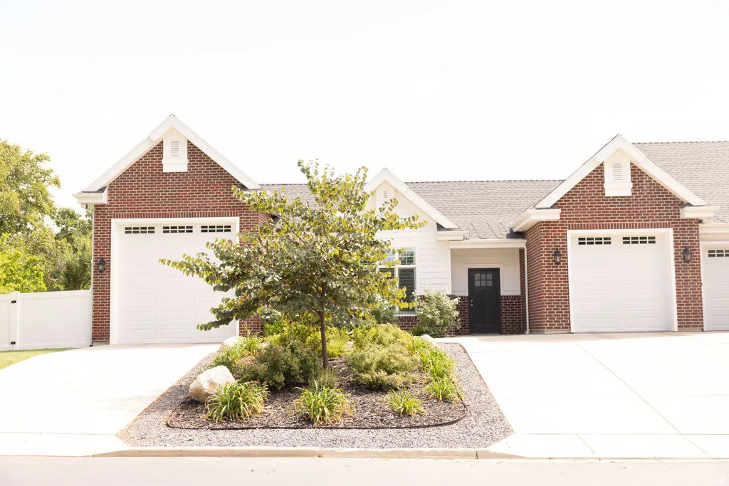 Brick and siding exterior featuring multiple white garage doors, a dark entry door, and a landscaped garden bed