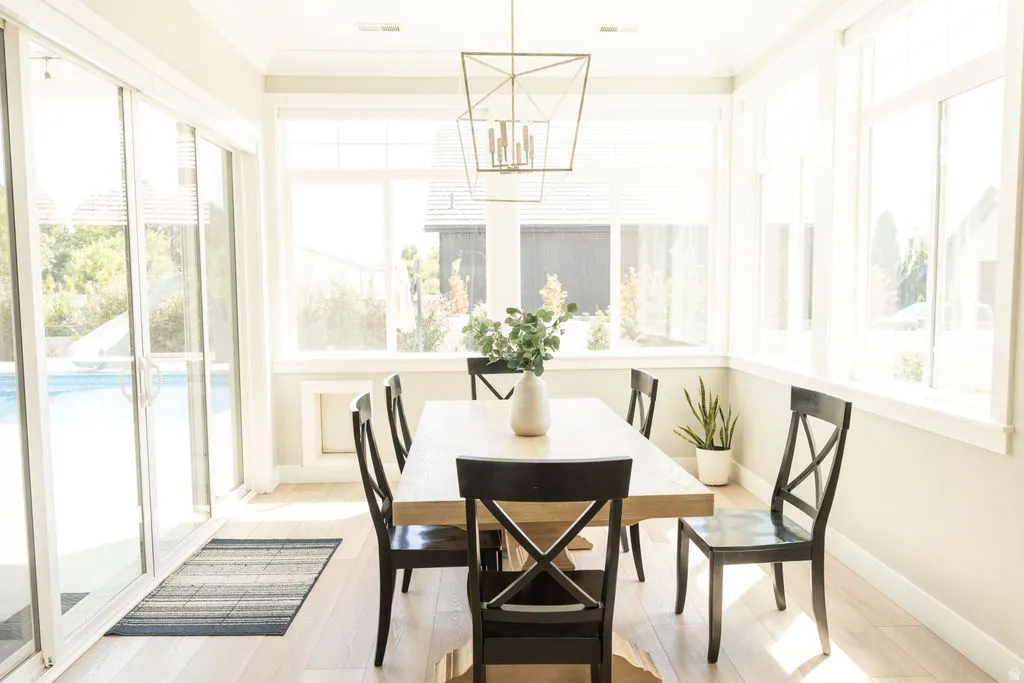 Light wood-finish flooring, expansive windows, multiple sliding glass doors, and a geometric chandelier