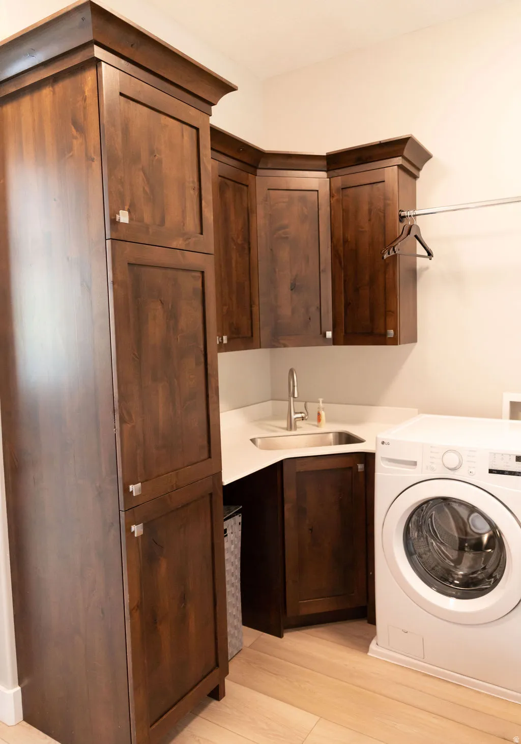 Built-in cabinetry with crown molding, corner sink with stainless steel faucet, light-toned countertop, and wood-finish flooring