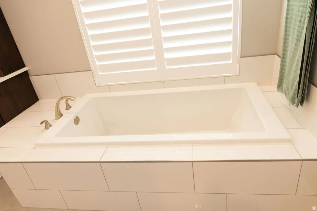 Built-in soaking tub with a tiled surround, brushed nickel fixtures, and white plantation shutters