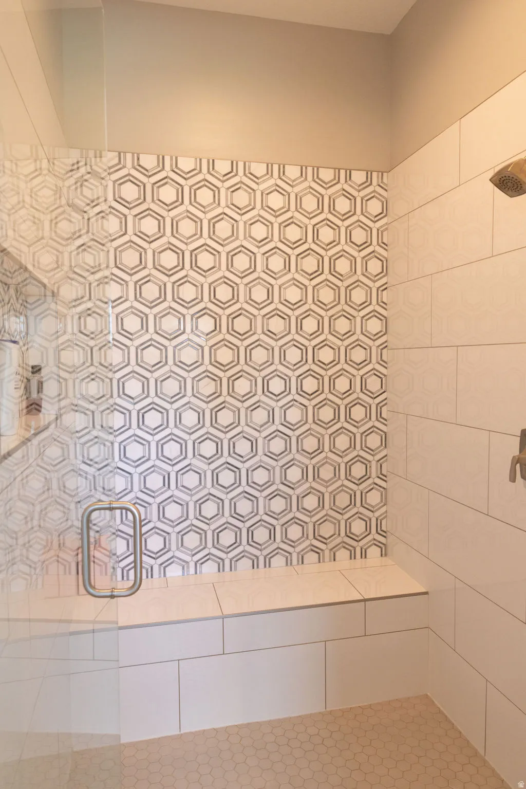 Glass-enclosed shower with a built-in bench, hexagon tile accent wall, white rectangular wall tiles, and hexagon floor tiles