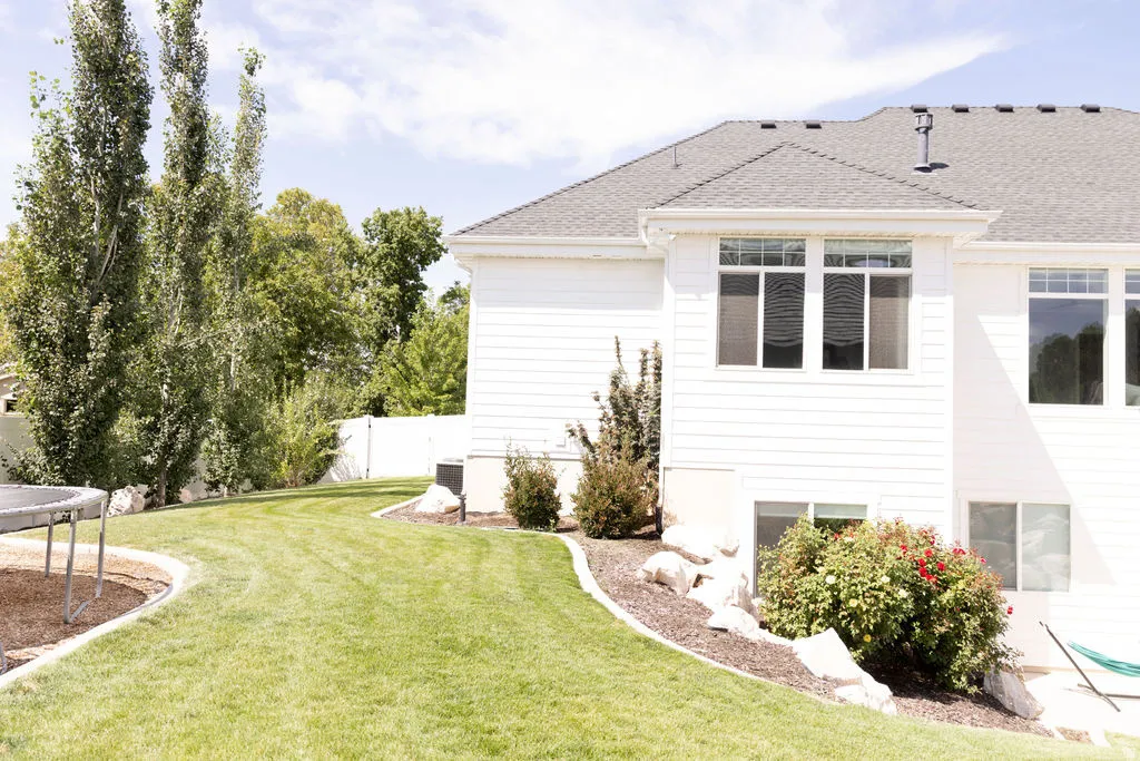 Expansive backyard featuring a manicured lawn, established landscaping, and a white privacy fence