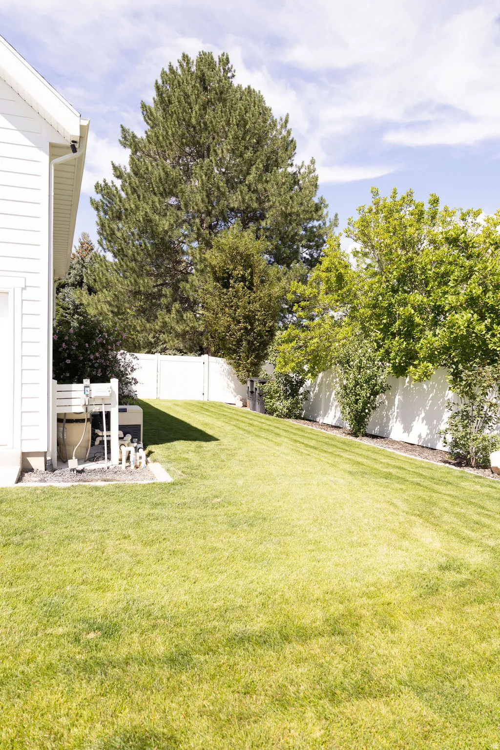 Expansive sloped lawn with mature trees and a white privacy fence