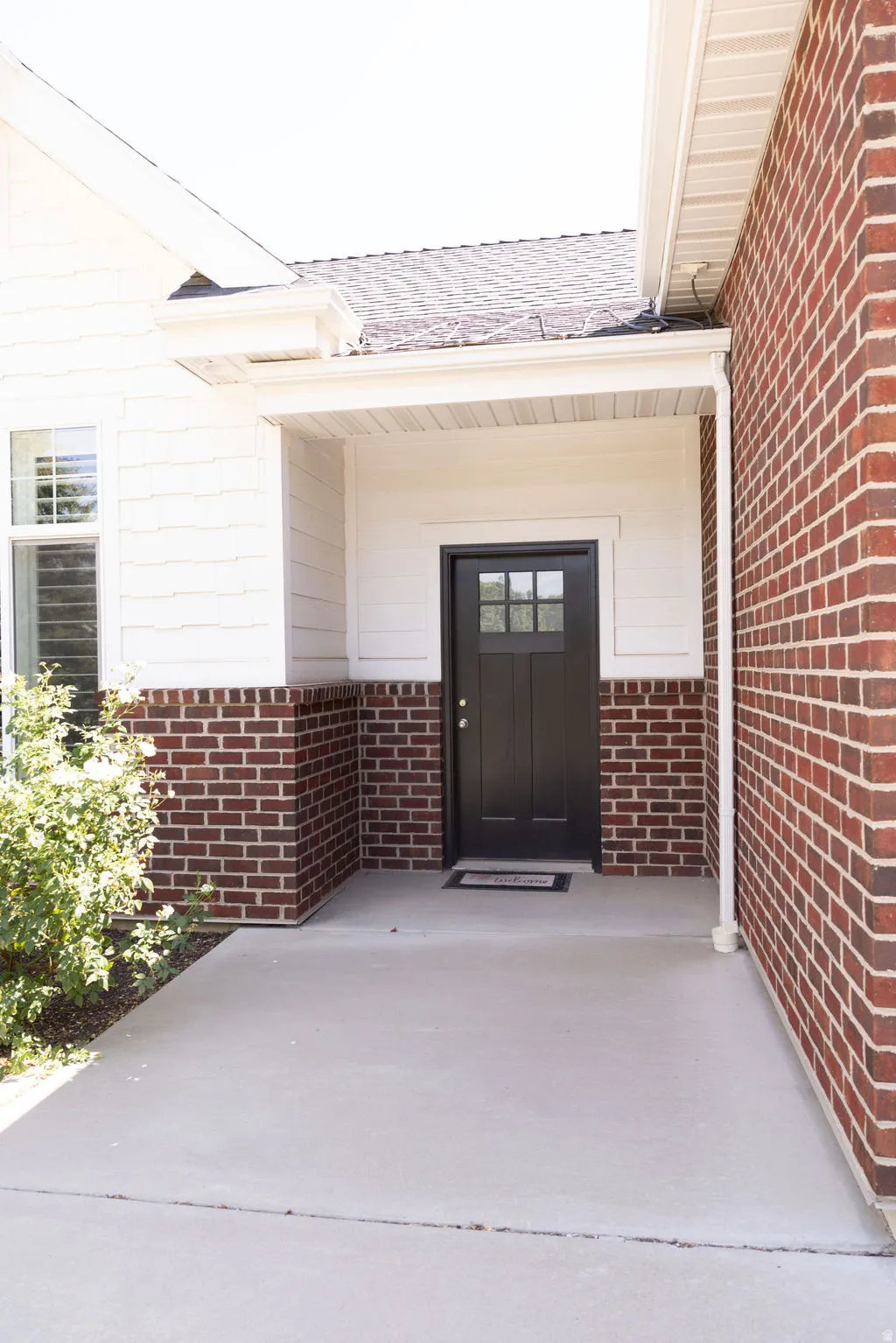Front entry featuring a black door with glass panes, brick and siding exterior, concrete porch, and white trim
