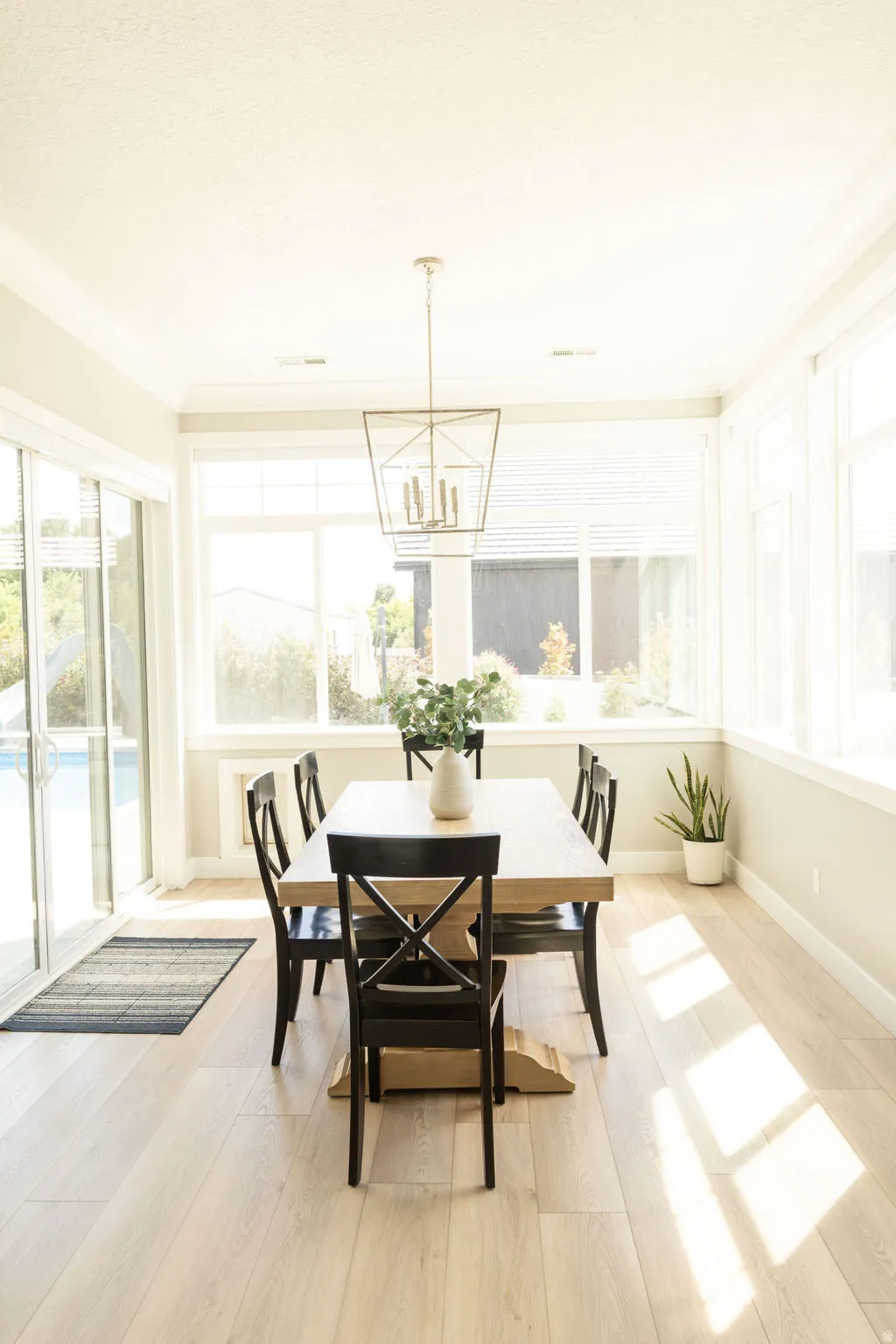 Light wood-finish flooring with expansive windows, a sliding glass door, and a geometric chandelier
