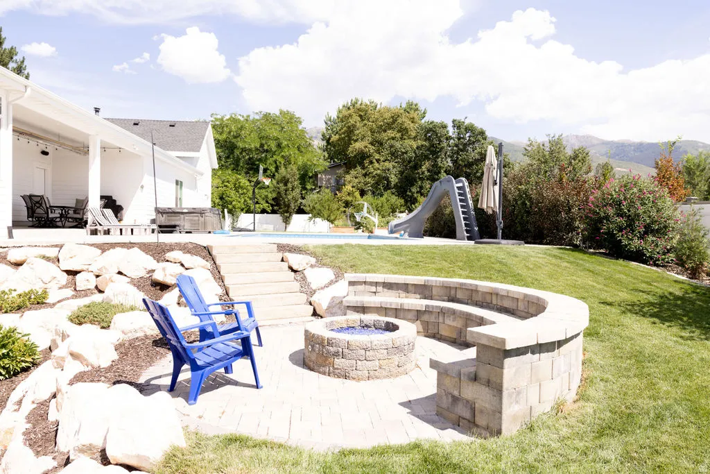 Paver patio with a built-in stone fire pit, tiered stone seating, and a rock landscaping wall