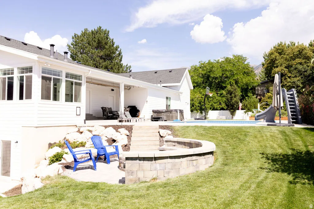 Expansive backyard featuring a swimming pool, integrated hot tub, covered patio, stone-faced fire pit, and terraced landscaping