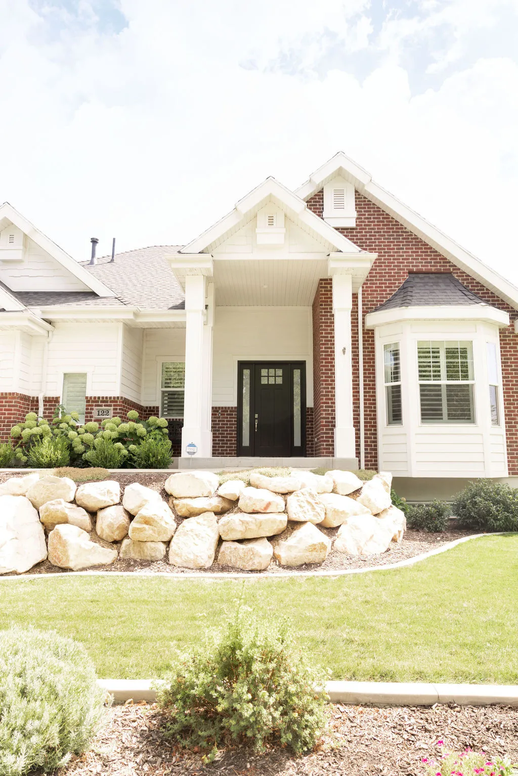 Exterior featuring a brick and siding facade, covered entry with columns, bay window, and a stone retaining wall
