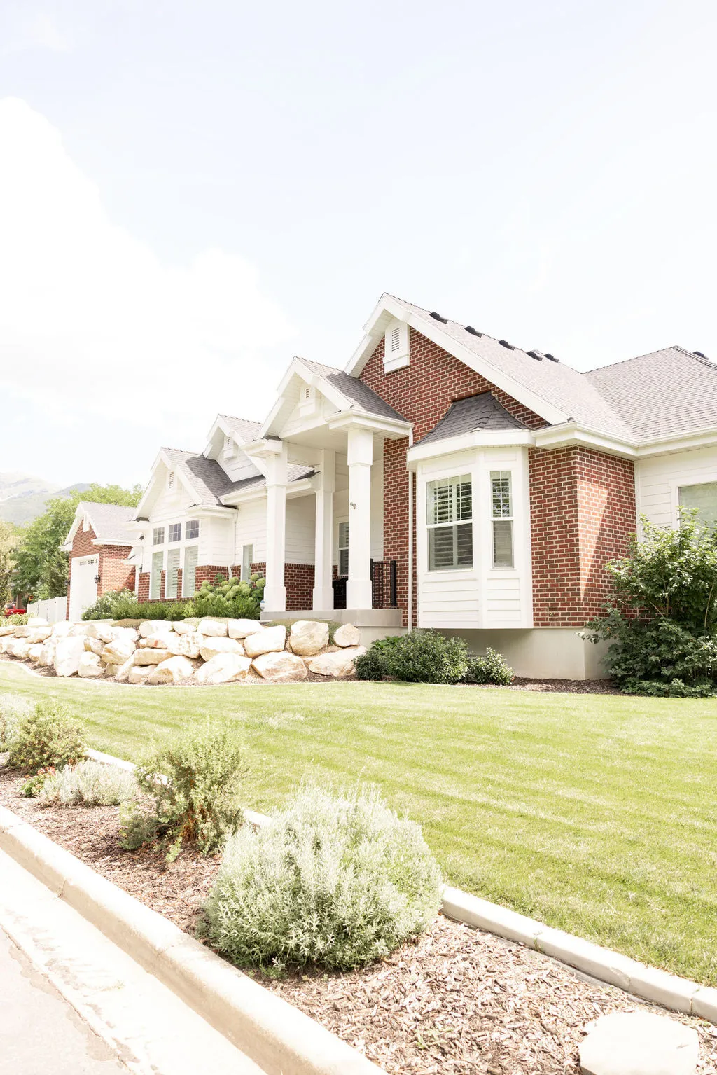 Brick and white siding exterior with a covered entry, bay window, gabled rooflines, and a manicured lawn