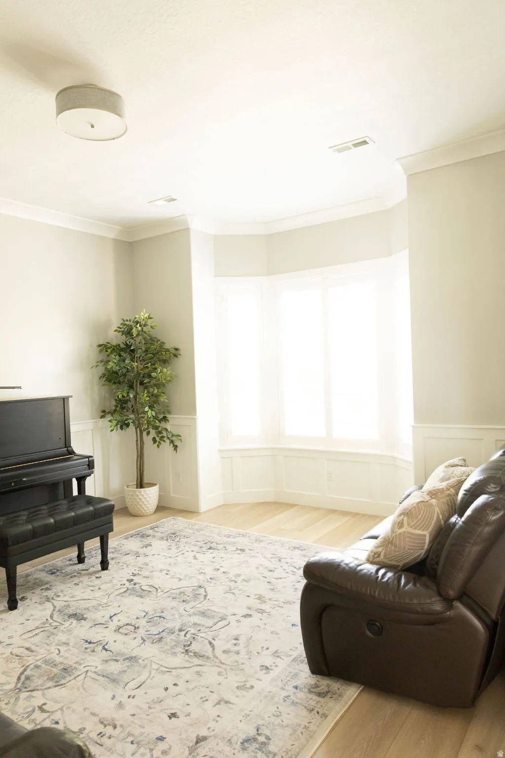 Bay window with integrated window seat, light wood-finish flooring, white wainscoting, and crown molding