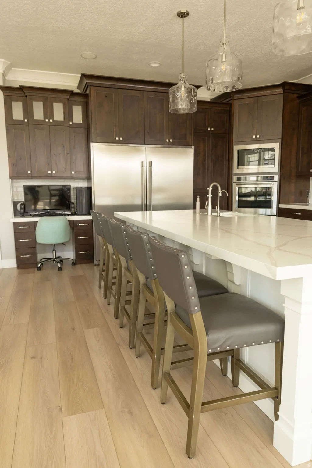 Light wood-finish flooring, dark wood cabinetry, stainless steel appliances, white countertop island, and built-in desk area