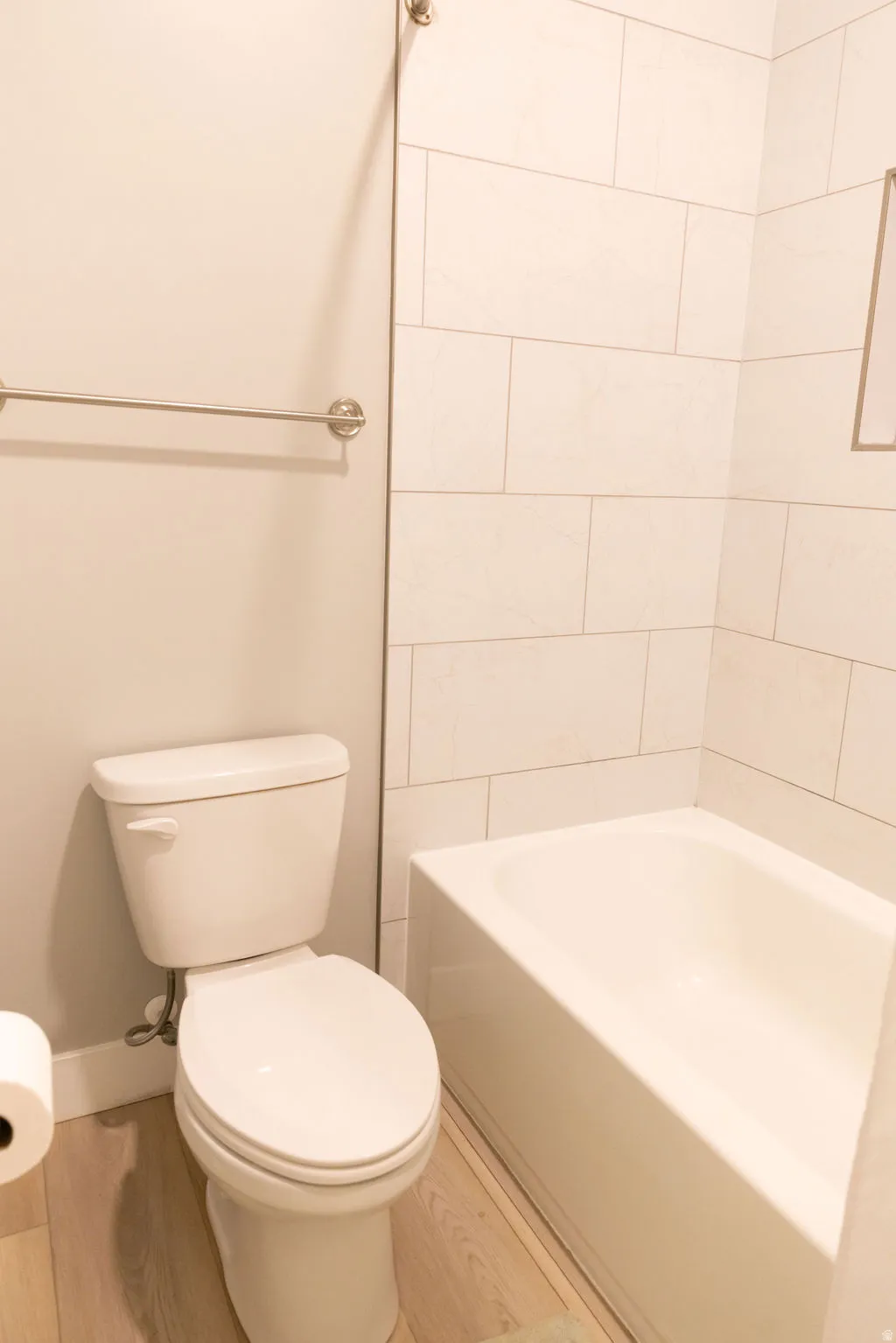 Built-in bathtub with subway tile surround, white toilet, and wood-finish flooring