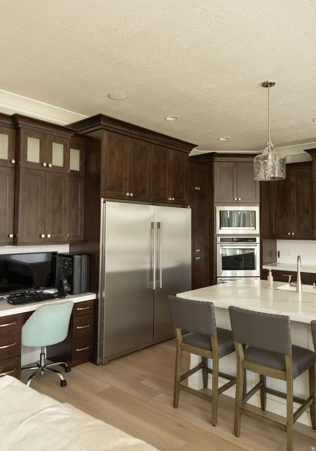 Stainless steel refrigerator, built-in stainless steel appliances, wood-finish flooring, dark wood-finish cabinetry, and a central island with countertop seating