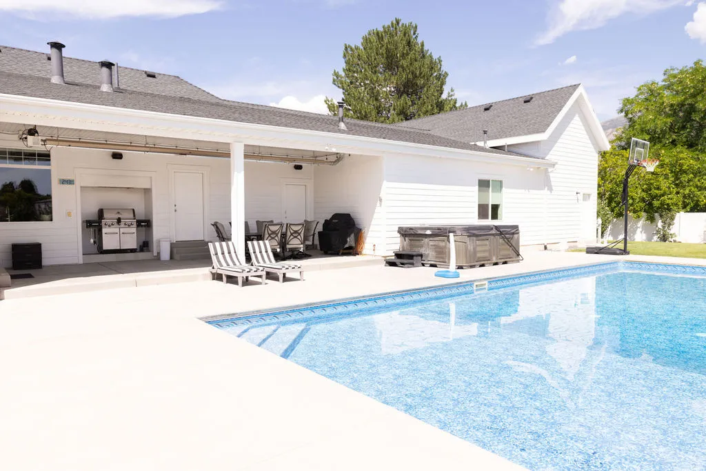 Outdoor swimming pool with integrated steps, expansive concrete patio, and a covered outdoor living area
