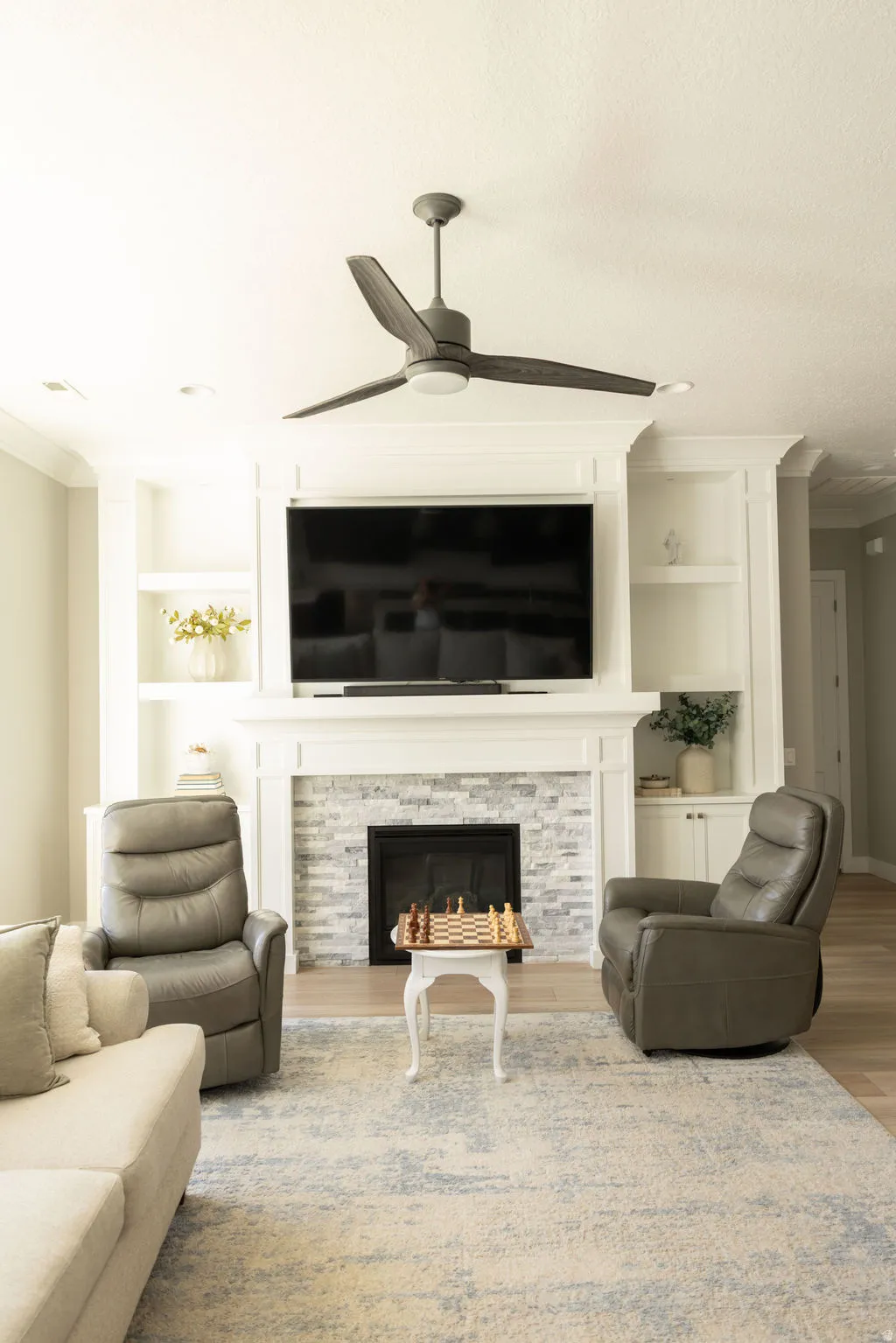 Built-in cabinetry flanking a fireplace with a stone surround, a white mantel, and a ceiling fan with integrated lighting