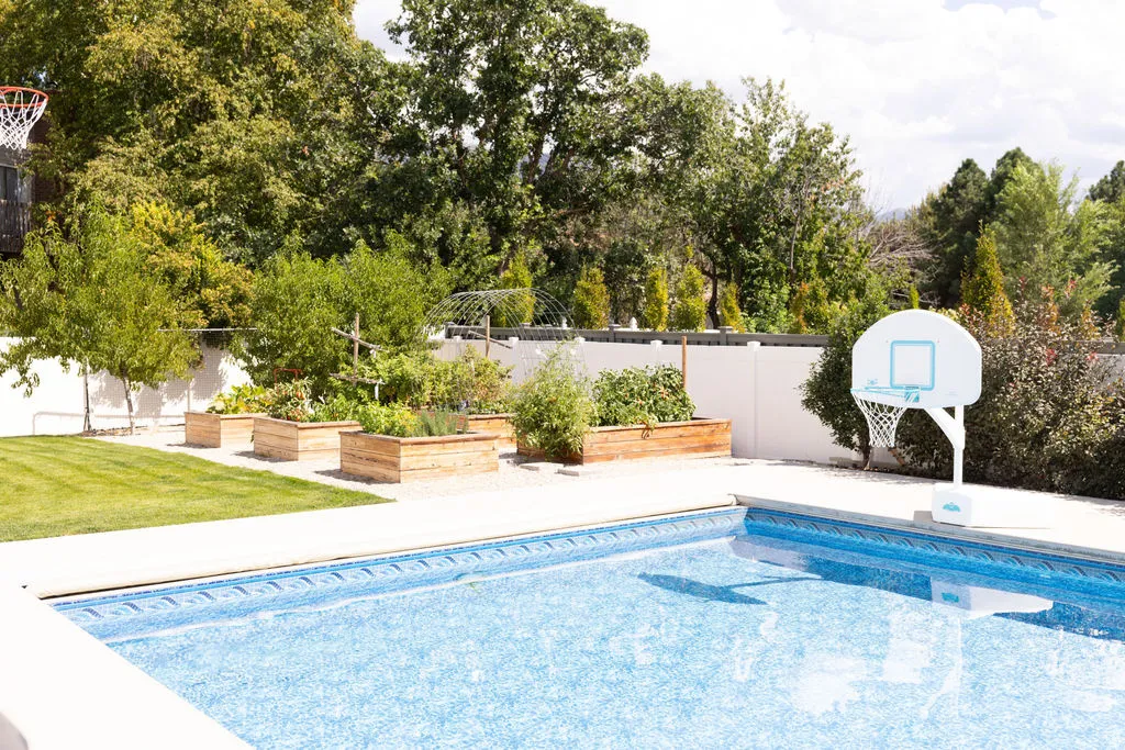 Outdoor swimming pool with a surrounding hardscape, manicured lawn, and raised garden beds
