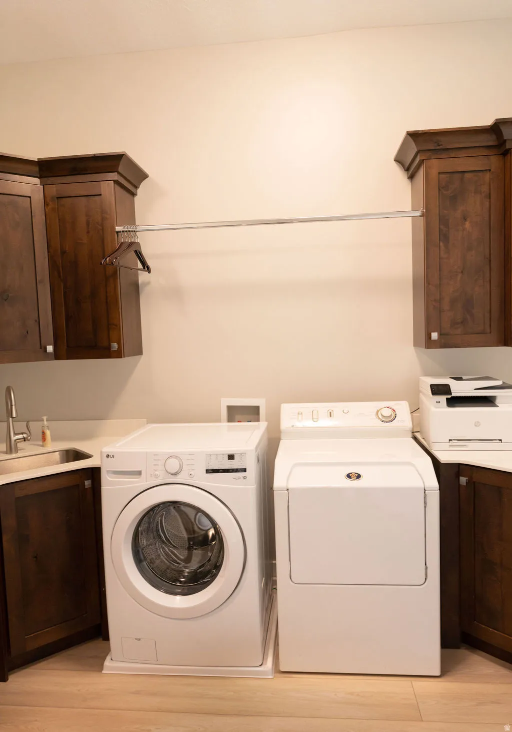 Built-in wood cabinetry with crown molding, stainless steel sink, light-toned countertop, and wood-finish flooring