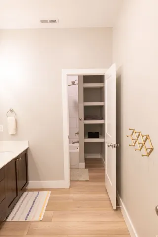 Wood-finish flooring throughout, vanity with integrated sink and countertop, built-in shelving, and a separate room with a tub and shower combination
