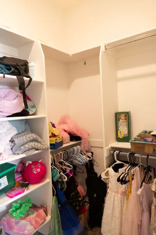 Walk-in closet featuring white built-in shelving, white walls, and multiple hanging rods