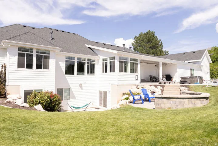Expansive backyard featuring a manicured lawn, stone retaining wall, and a raised patio with a covered outdoor area