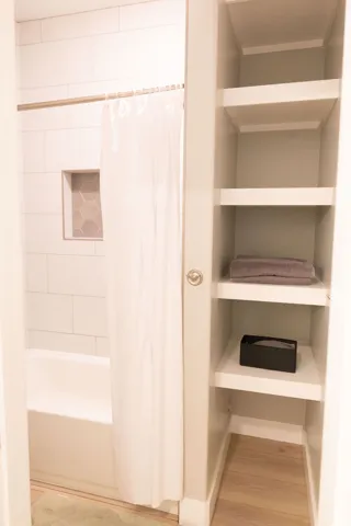 White subway tile shower surround with a built-in hexagonal tile niche, a white soaking tub, and custom built-in shelving with wood-finish flooring