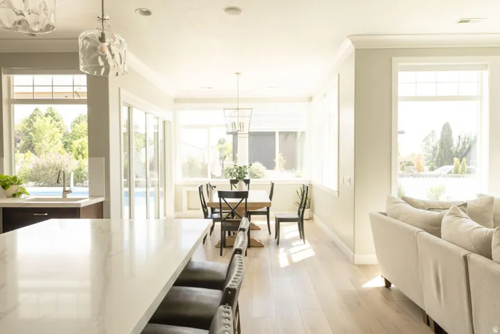 Open-concept living space with light wood-finish flooring, a kitchen island featuring a light-toned countertop, and multiple large windows