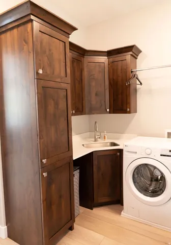 Built-in cabinetry with crown molding, corner sink with stainless steel faucet, light-toned countertop, and wood-finish flooring