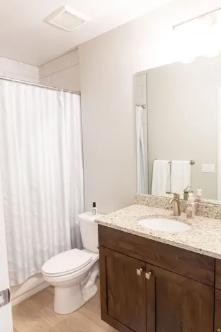 Wood-finish flooring, white subway tile shower surround, wood vanity with brushed nickel hardware, light-toned countertop, and undermount sink