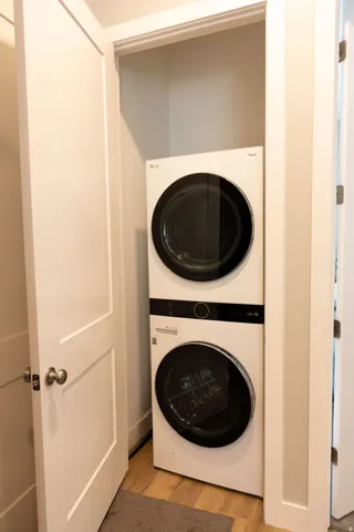 Stacked washer and dryer unit within a dedicated closet, featuring a paneled door and wood-finish flooring