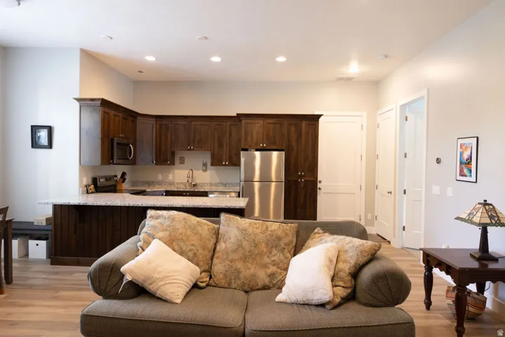 Open-concept living area with wood-finish flooring, recessed lighting, and a kitchen featuring dark wood cabinetry, light-toned countertops, and stainless steel appliances