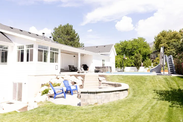Expansive tiered backyard featuring a swimming pool, stone fire pit, and a covered patio area