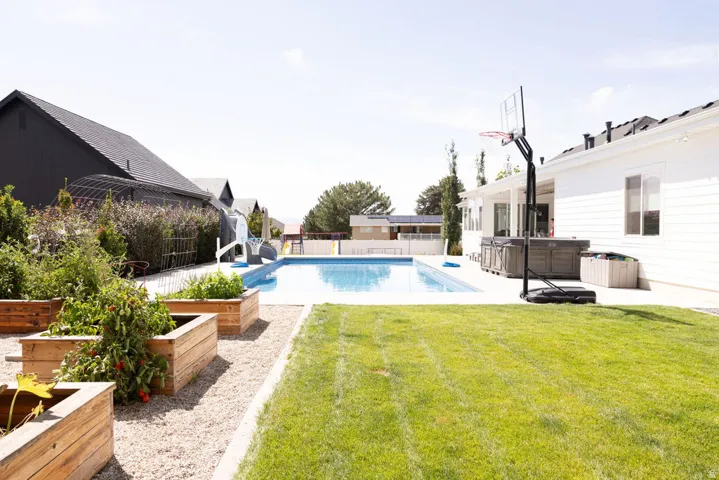 Backyard featuring a swimming pool, concrete patio, a grass lawn, and multiple raised garden beds