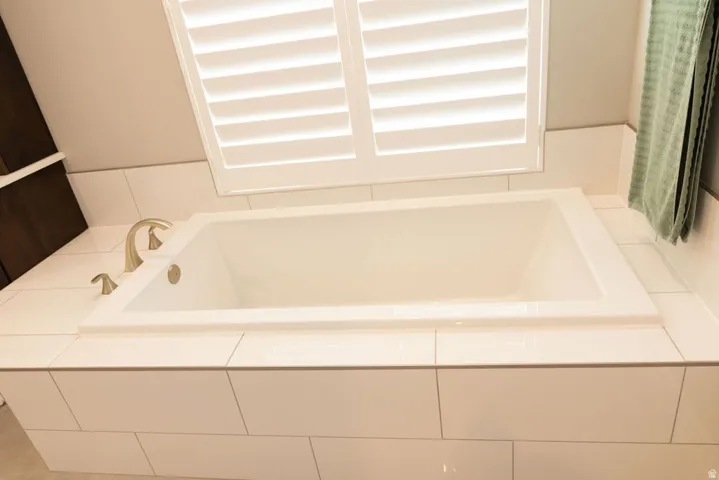 Built-in soaking tub with a tiled surround, brushed nickel fixtures, and white plantation shutters