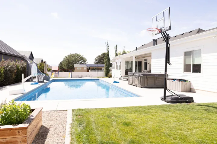 Expansive backyard featuring a rectangular swimming pool, concrete patio, covered porch, and manicured lawn