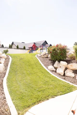 Expansive backyard featuring a manicured lawn, established landscaping, decorative boulders, and a privacy fence