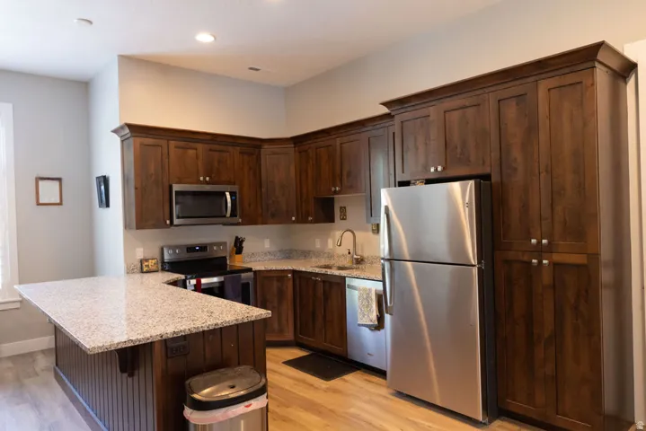 Kitchen featuring wood-finish cabinetry, stainless steel appliances, a corner island with a granite countertop, and wood-finish flooring