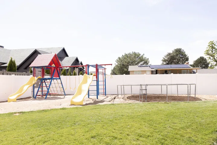 Expansive green lawn, white perimeter fencing, and a dedicated play area with a sand base