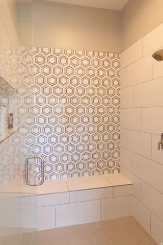 Glass-enclosed shower with a built-in bench, hexagon tile accent wall, white rectangular wall tiles, and hexagon floor tiles