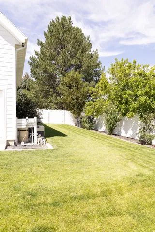 Expansive sloped lawn with mature trees and a white privacy fence