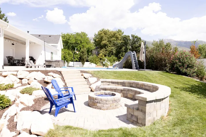 Paver patio with a built-in stone fire pit, tiered stone seating, and a rock landscaping wall