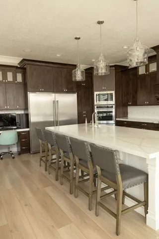 Expansive kitchen island with a white countertop, dark wood cabinetry, stainless steel appliances, wood-finish flooring, and pendant lighting