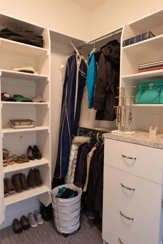 Built-in closet system featuring white shelving, multiple hanging rods, and a white dresser with contemporary pull handles and a light-toned countertop