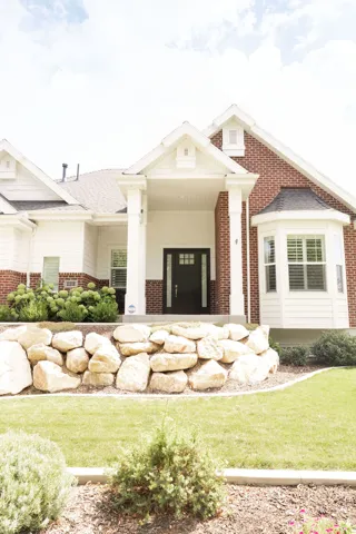Exterior featuring a brick and siding facade, covered entry with columns, bay window, and a stone retaining wall