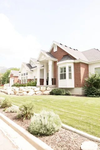 Brick and white siding exterior with a covered entry, bay window, gabled rooflines, and a manicured lawn