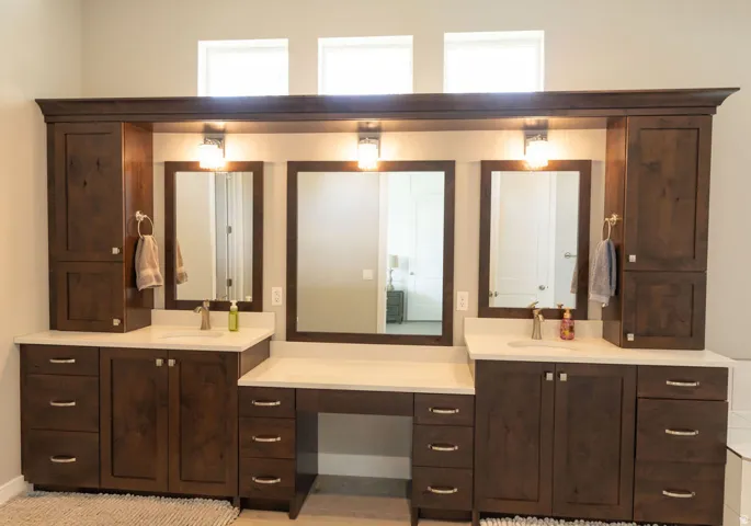 Dual vanity with integrated sinks, white countertops, dark wood-finish cabinetry, three rectangular mirrors, and overhead wall sconces
