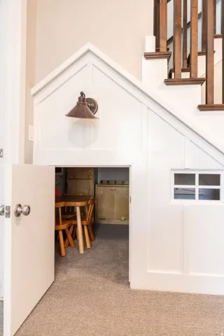 Custom built-in under-stair play area featuring a paneled facade, interior carpeting, and a decorative wall sconce