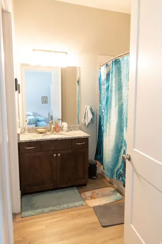 Bathroom with wood-finish flooring, a dark wood-finish vanity with a light-toned countertop, and a shower with a curved rod