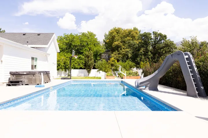 Outdoor swimming pool with integrated slide, surrounded by a concrete patio