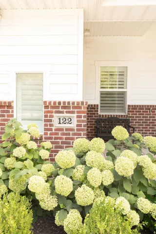 White siding exterior with brick foundation, contrasting window trim, and mature landscaping